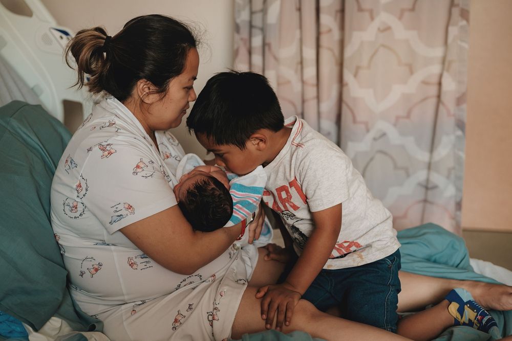 Family members cuddle together on a couch sharing a tender moment with a newborn baby at home.