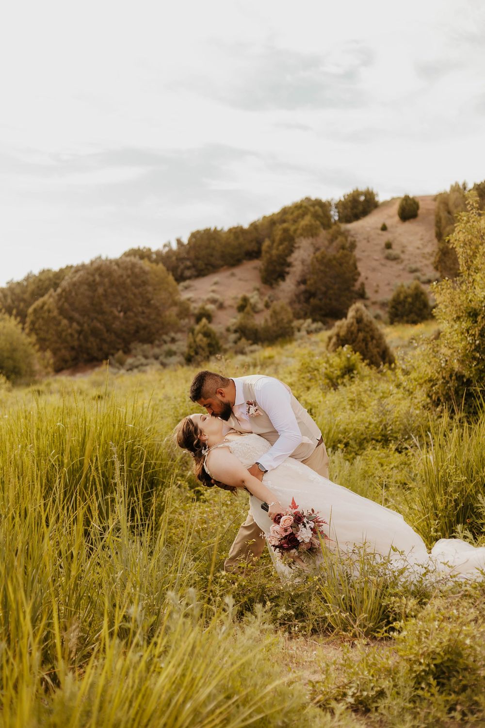 Romantic dip pose in meadow with wildflowers during golden hour wedding photography.