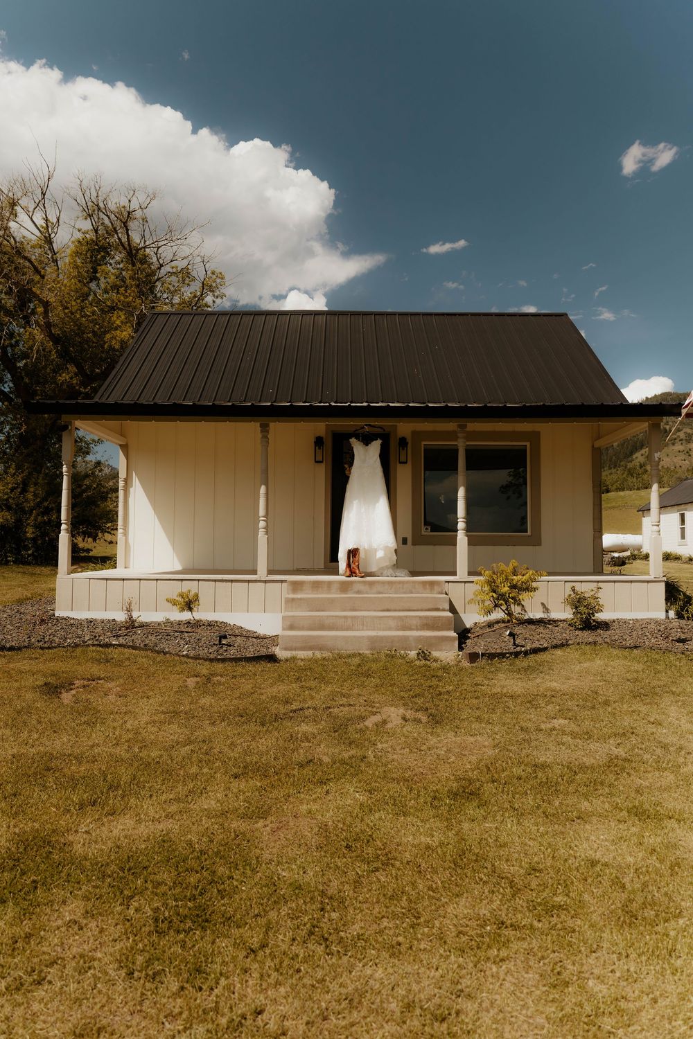 Modern white ranch house with black roof and covered porch on a grassy hillside.