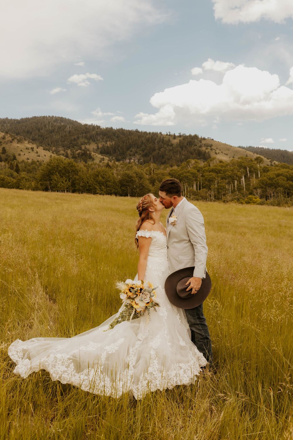 Western Couple in wedding attire sharing romantic moments in a sunlit mountain meadow.