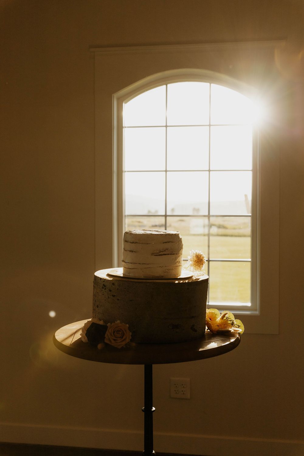 A wedding cake photographed in front of a bright window with natural sunlight creating a glowing silhouette effect.