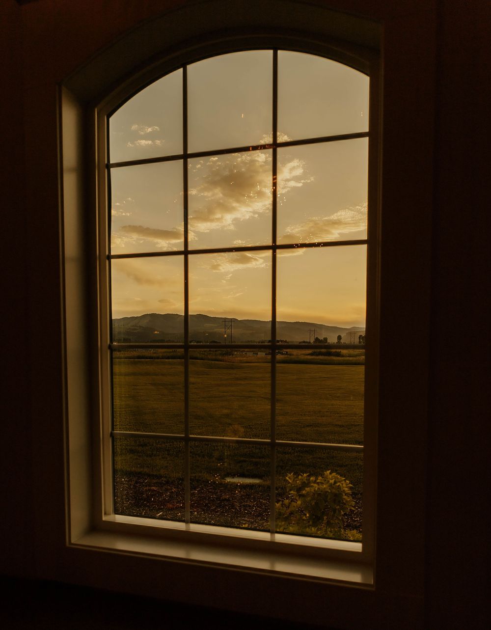 Scenic sunset view through arched windows overlooking rolling hills and countryside.