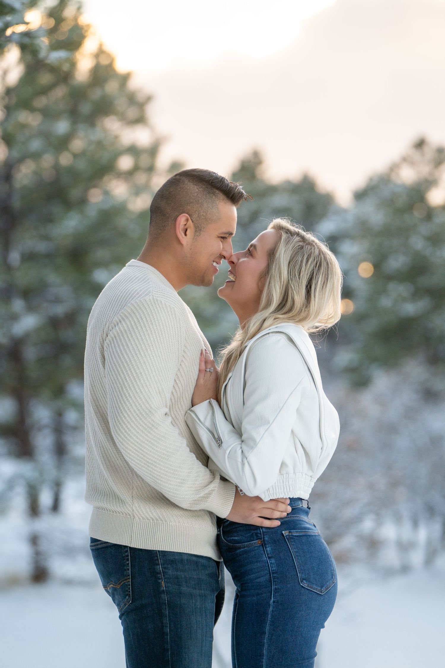 A romantic winter moment between a couple in cream sweaters against a snowy forest backdrop.