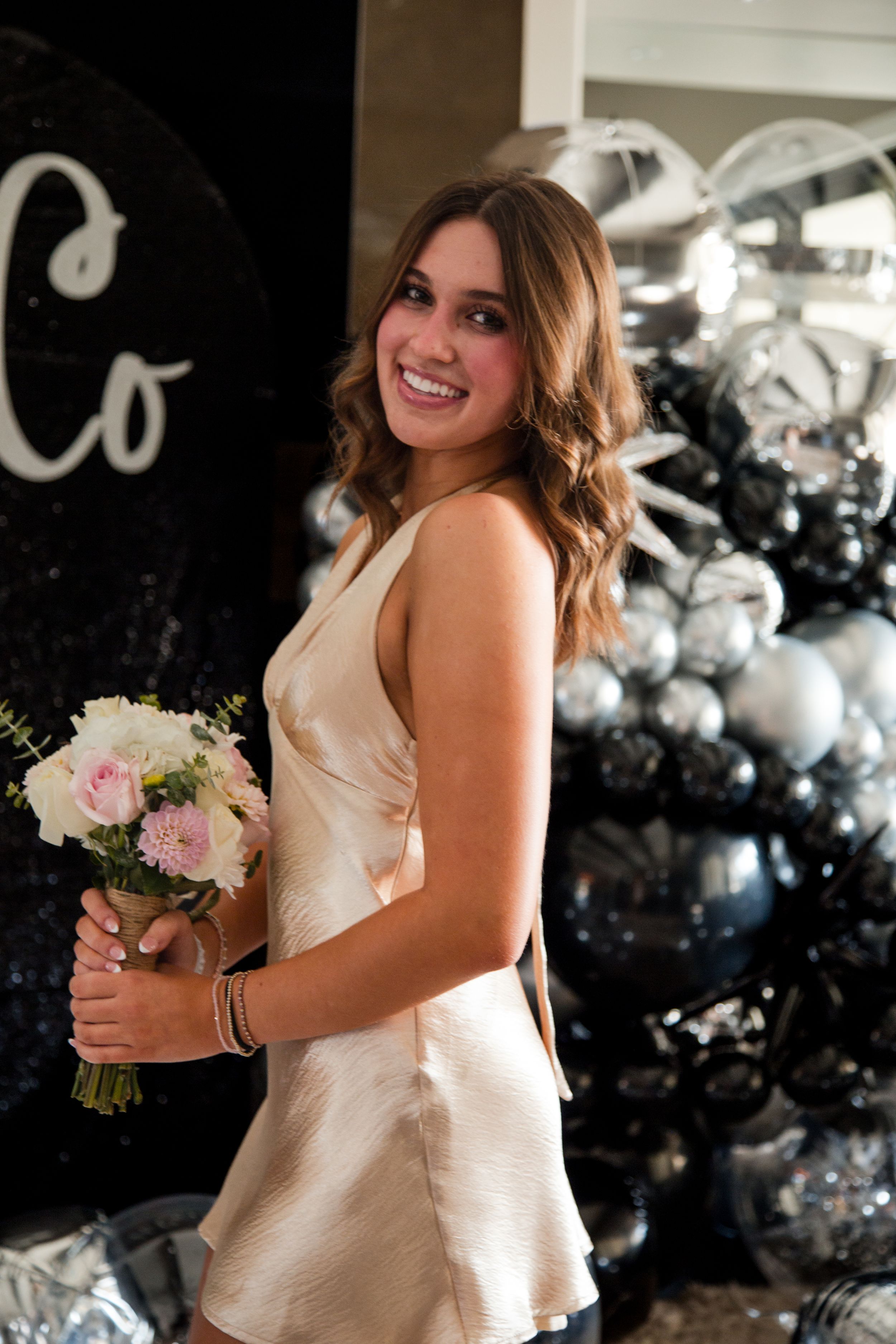 A homecoming gold dress girl holds a pink and white bouquet while posing against a dark backdrop with silver decorations. sacramento photos