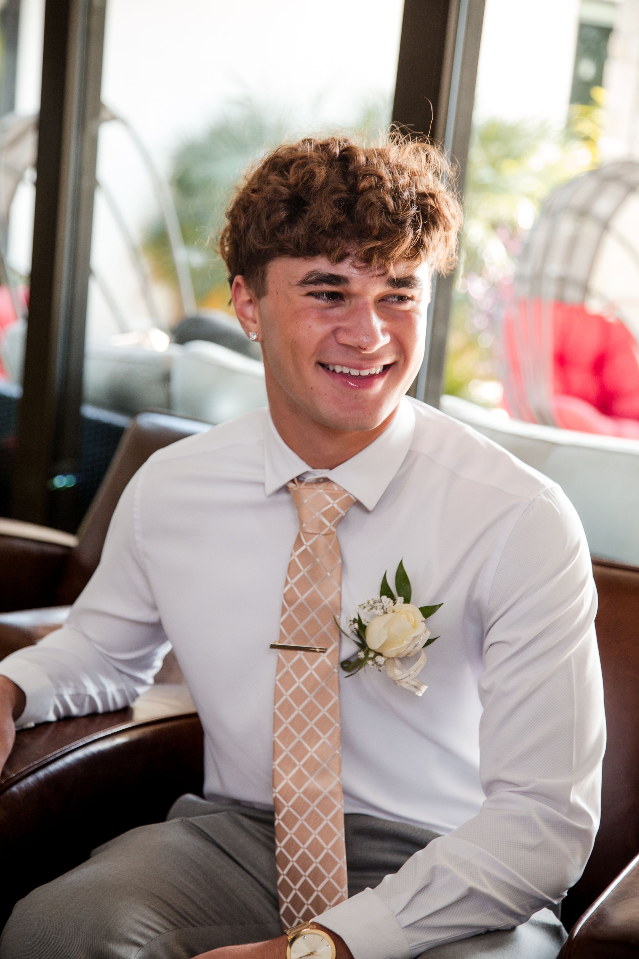 Young attendee in formal attire with white dress shirt, patterned tie and boutonniere sits smiling. sacramento homecoming