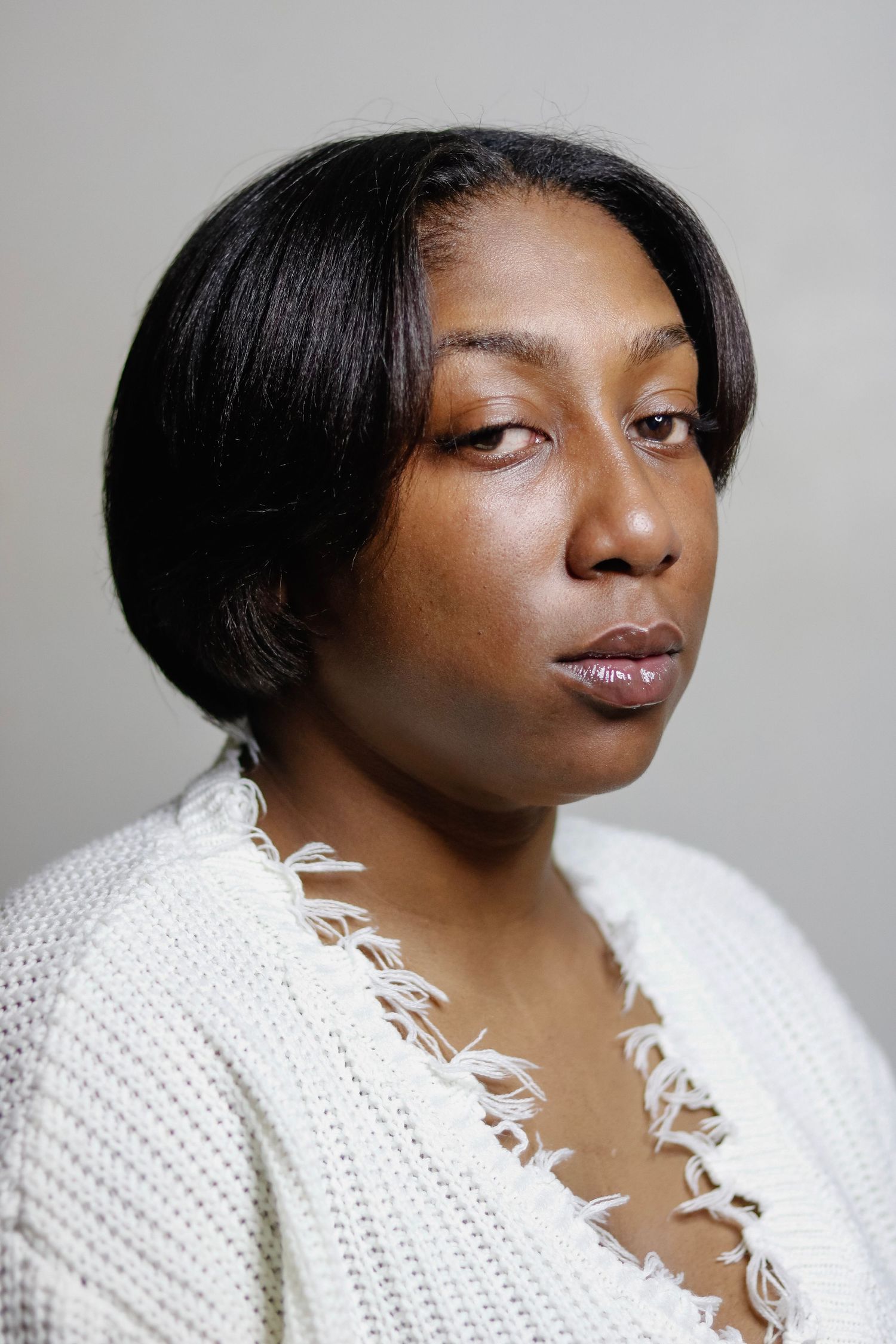 Side profile portrait of a person wearing a white knit sweater with feather accents.
