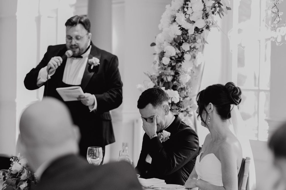Wedding guests enjoy a candid moment during a reception at an elegant white-decorated venue.