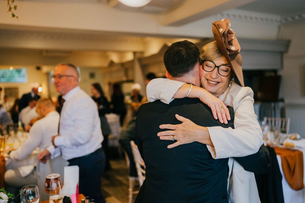 Wedding guests share emotional embraces during a heartfelt reception celebration in an indoor venue.
