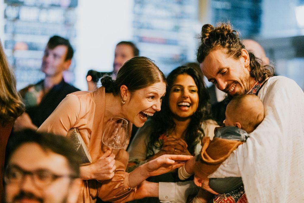 Group of people laughing and having fun together at a social gathering with warm lighting and joyful expressions.
