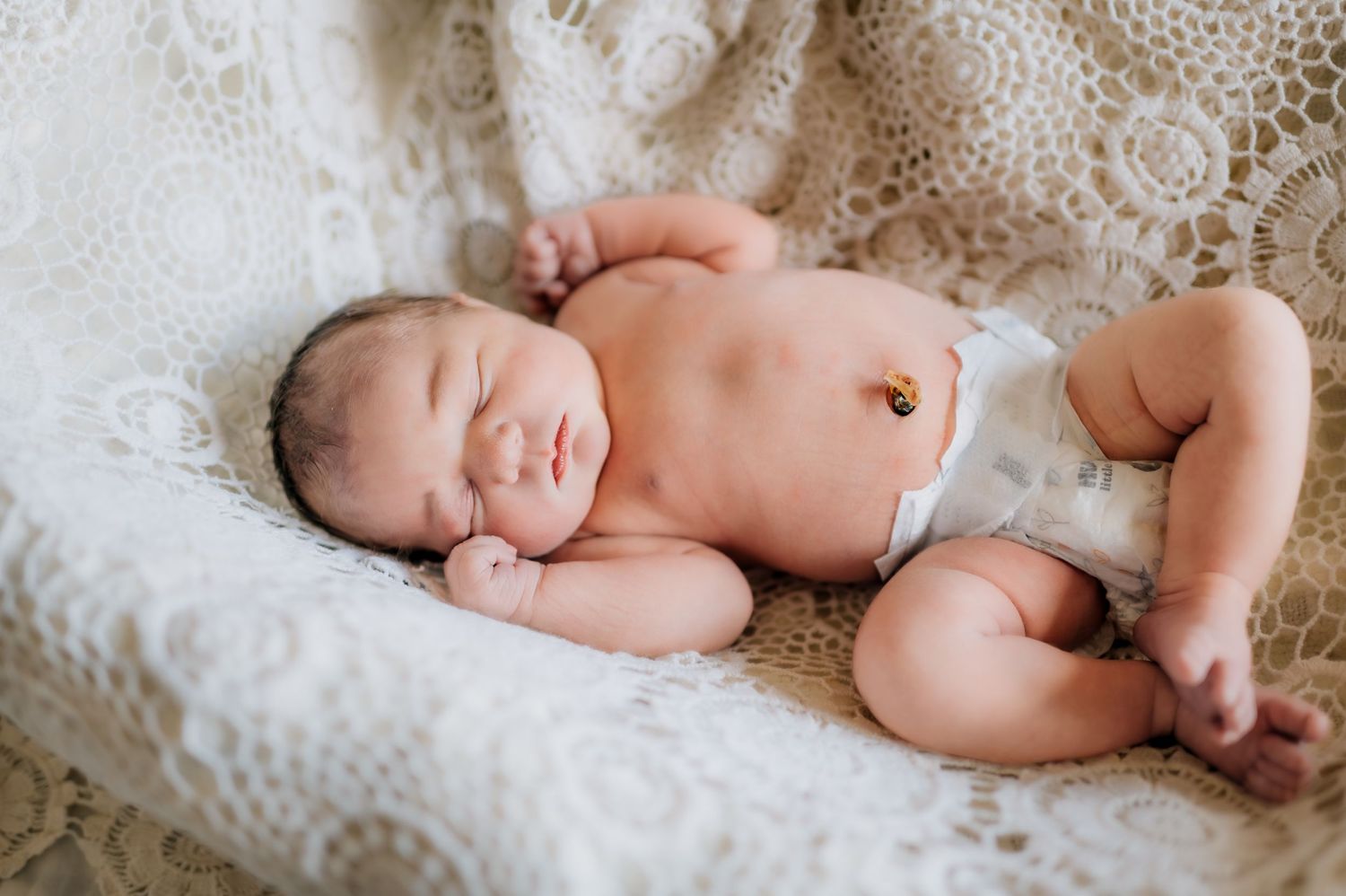 A sleeping newborn baby lies peacefully on white lace bedding.