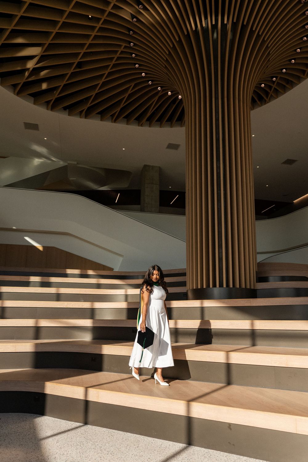 Woman in white dress poses on wooden steps inside modern building with striking ribbed column and curved ceiling.