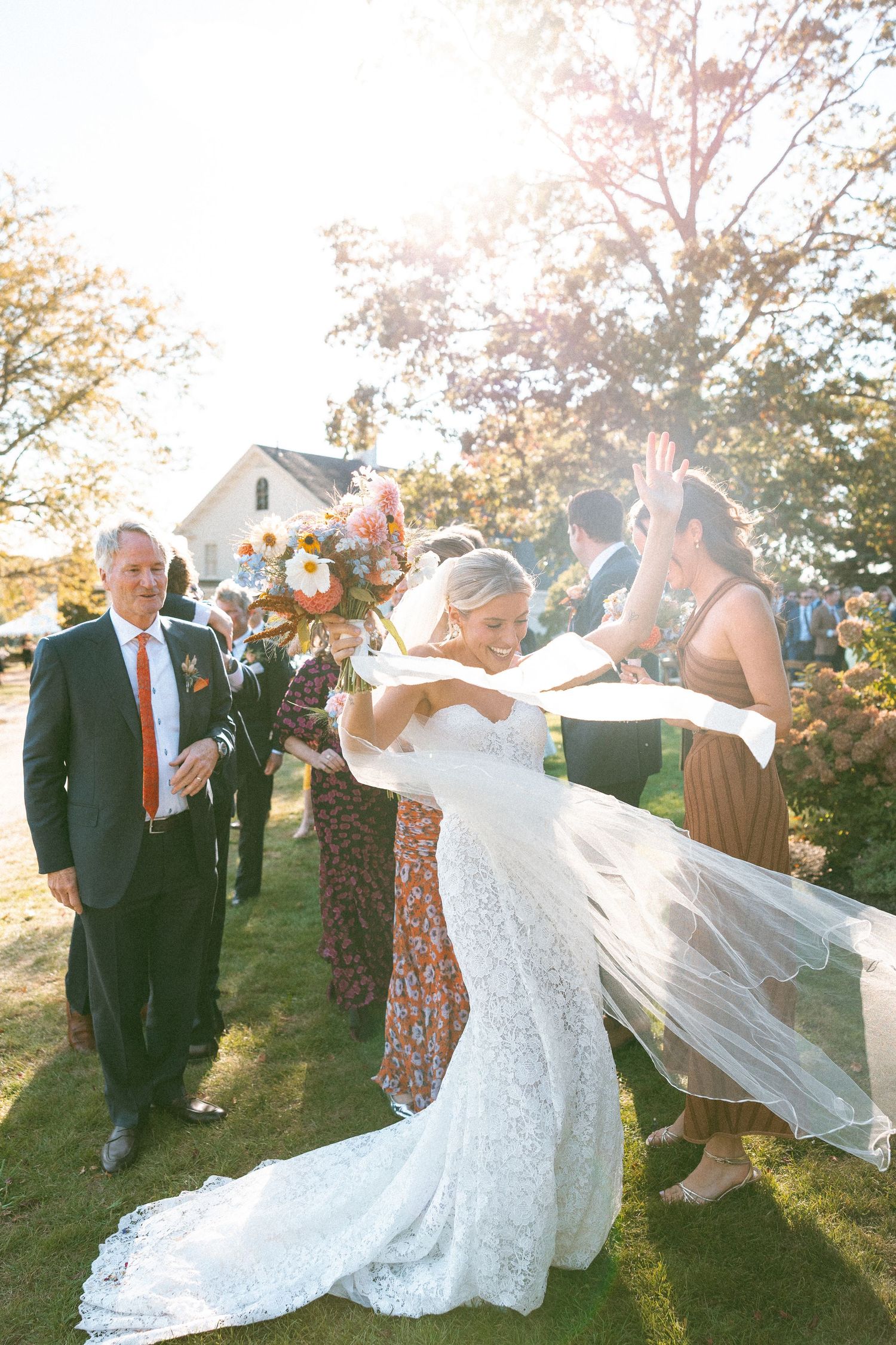 Wedding couple playfully posing with flowing veil in golden afternoon light.