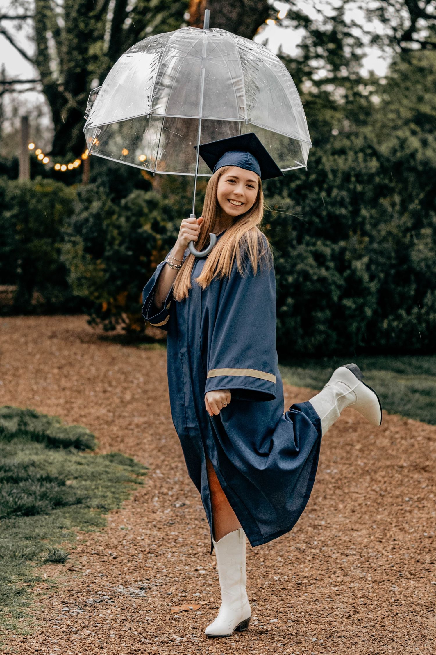 A person twirls joyfully while holding a clear umbrella in a navy poncho and white boots on a fall forest path.
