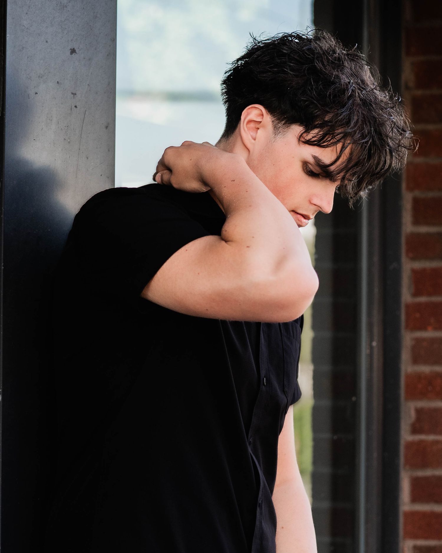 A figure in a black shirt stands in a dramatic pose against a brick wall with natural lighting.