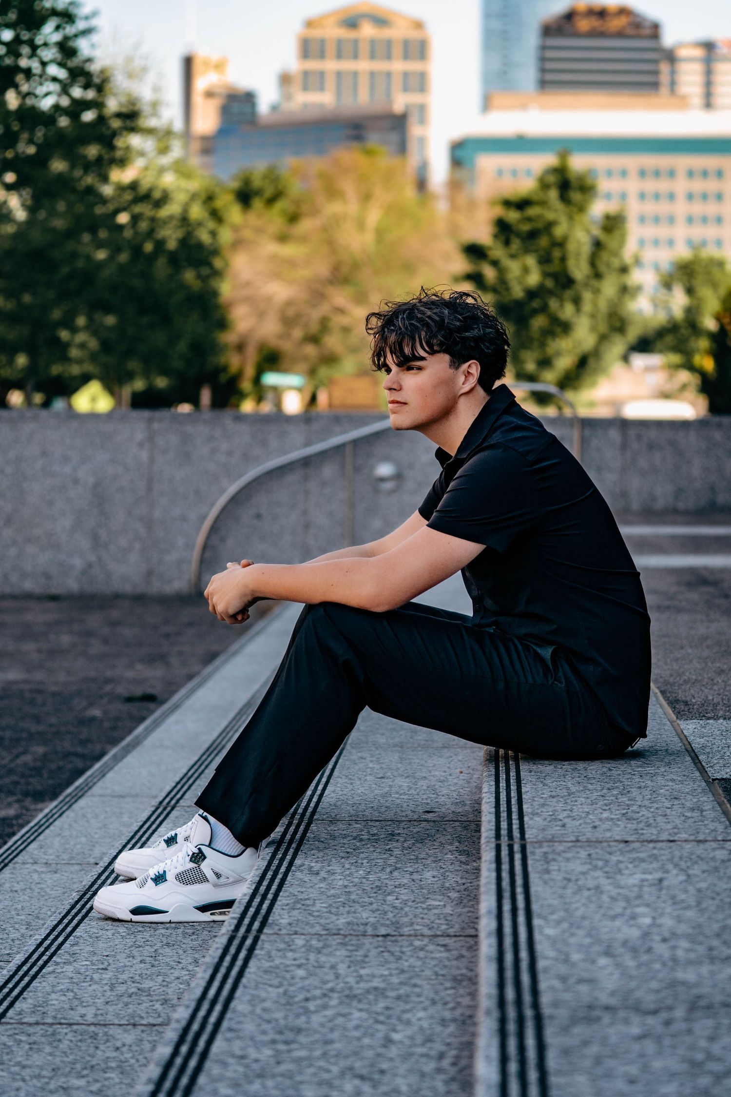 Person in black outfit sits on concrete steps with city buildings in background during golden hour.