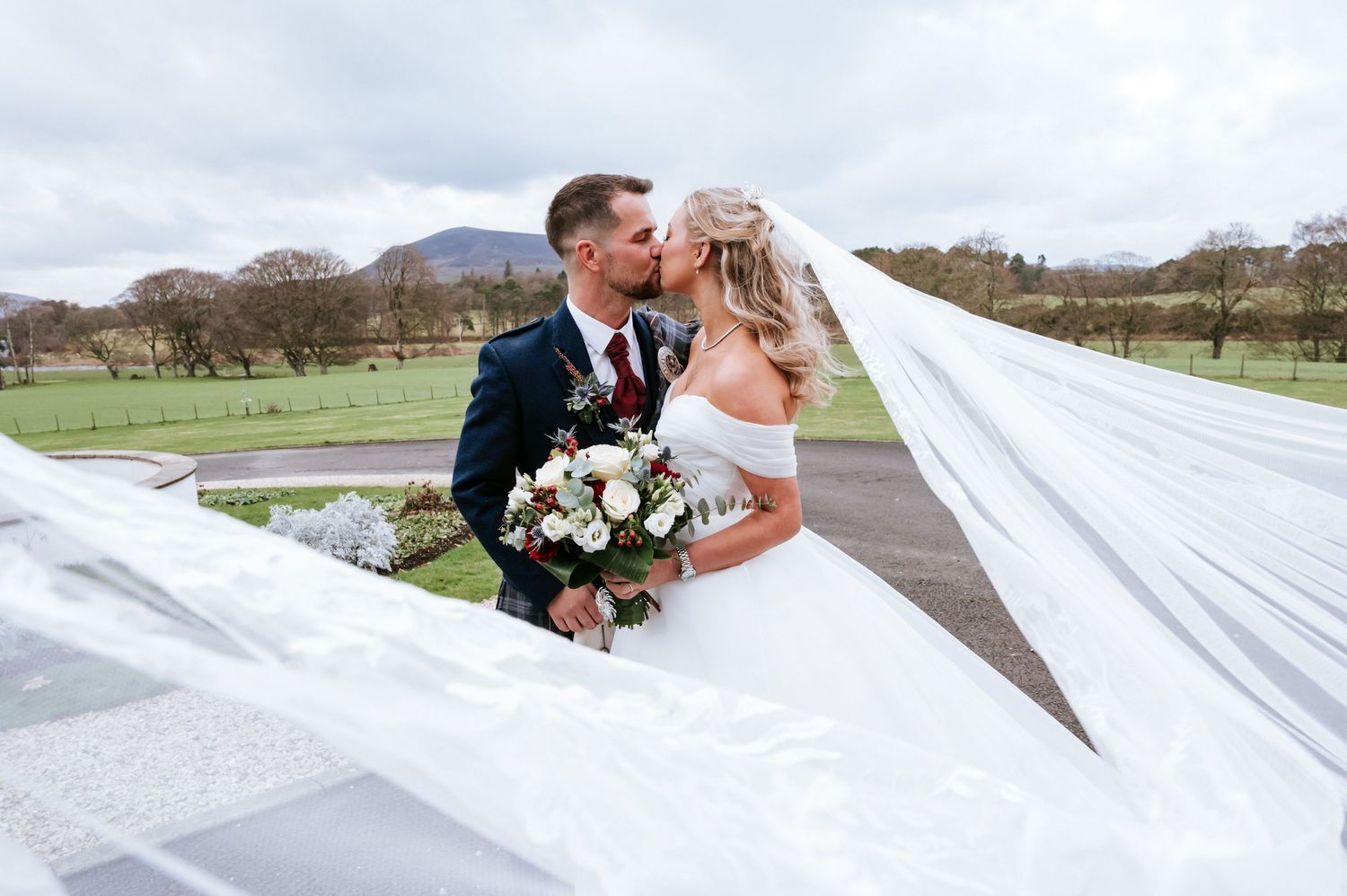 White flowing wedding veil captured in motion during ceremony under ornate garden gazebo.