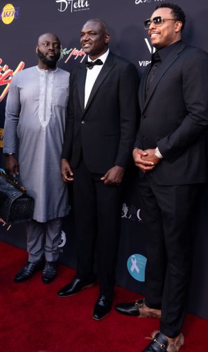 Three guests in formal attire pose together on a red carpet at an event.