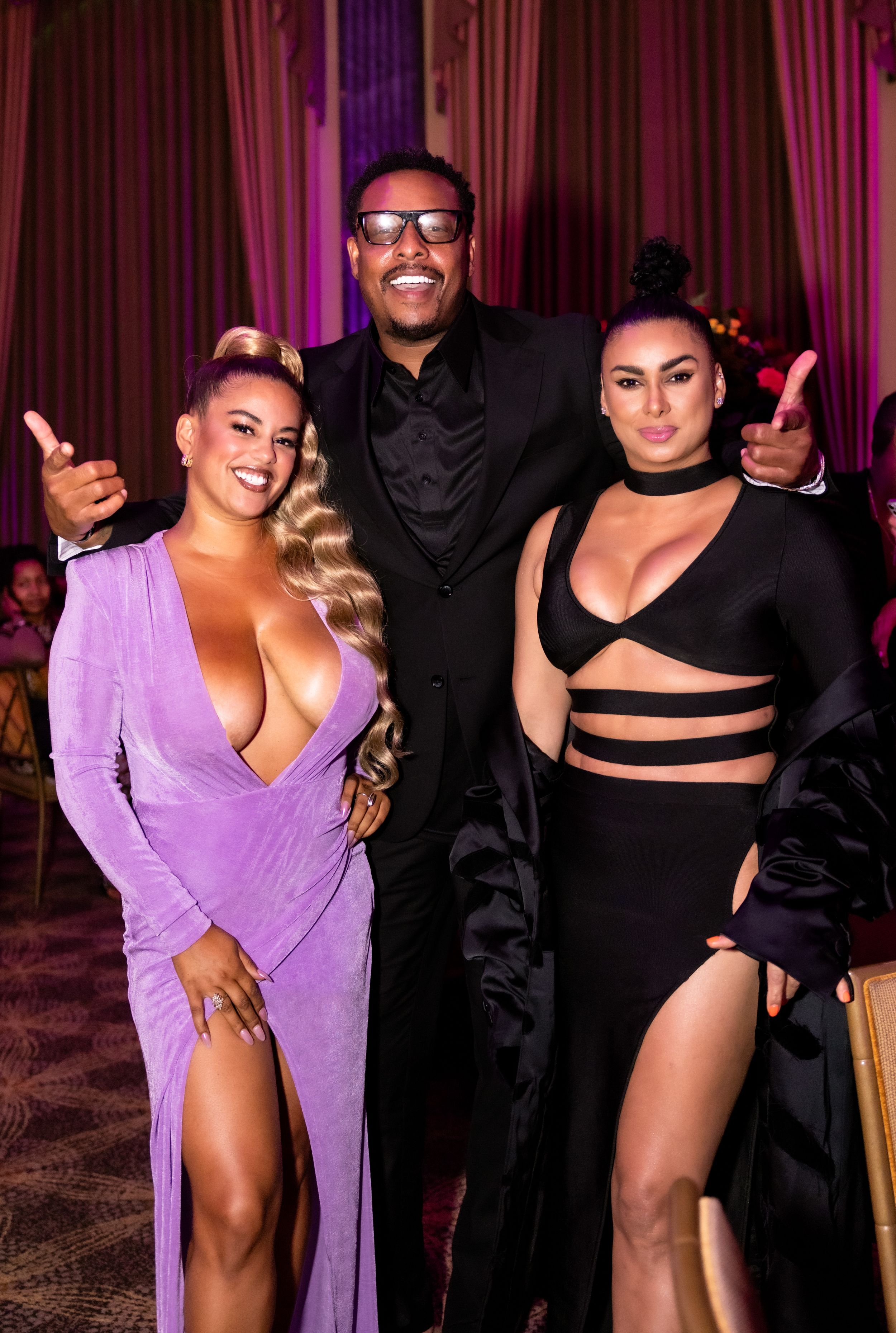 Three attendees pose together at an elegant evening event with red curtain backdrop.