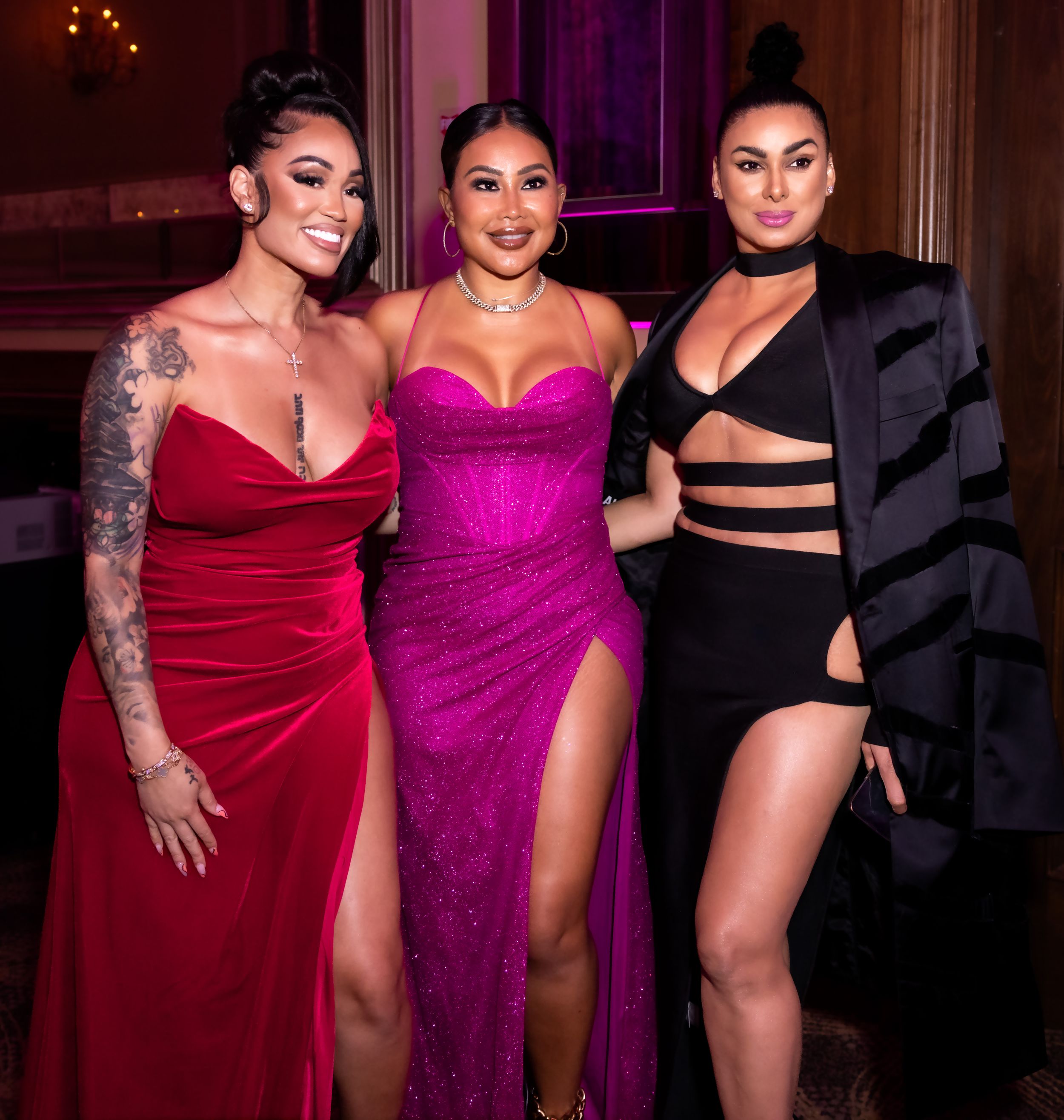 Three women pose together in glamorous evening gowns at formal event.