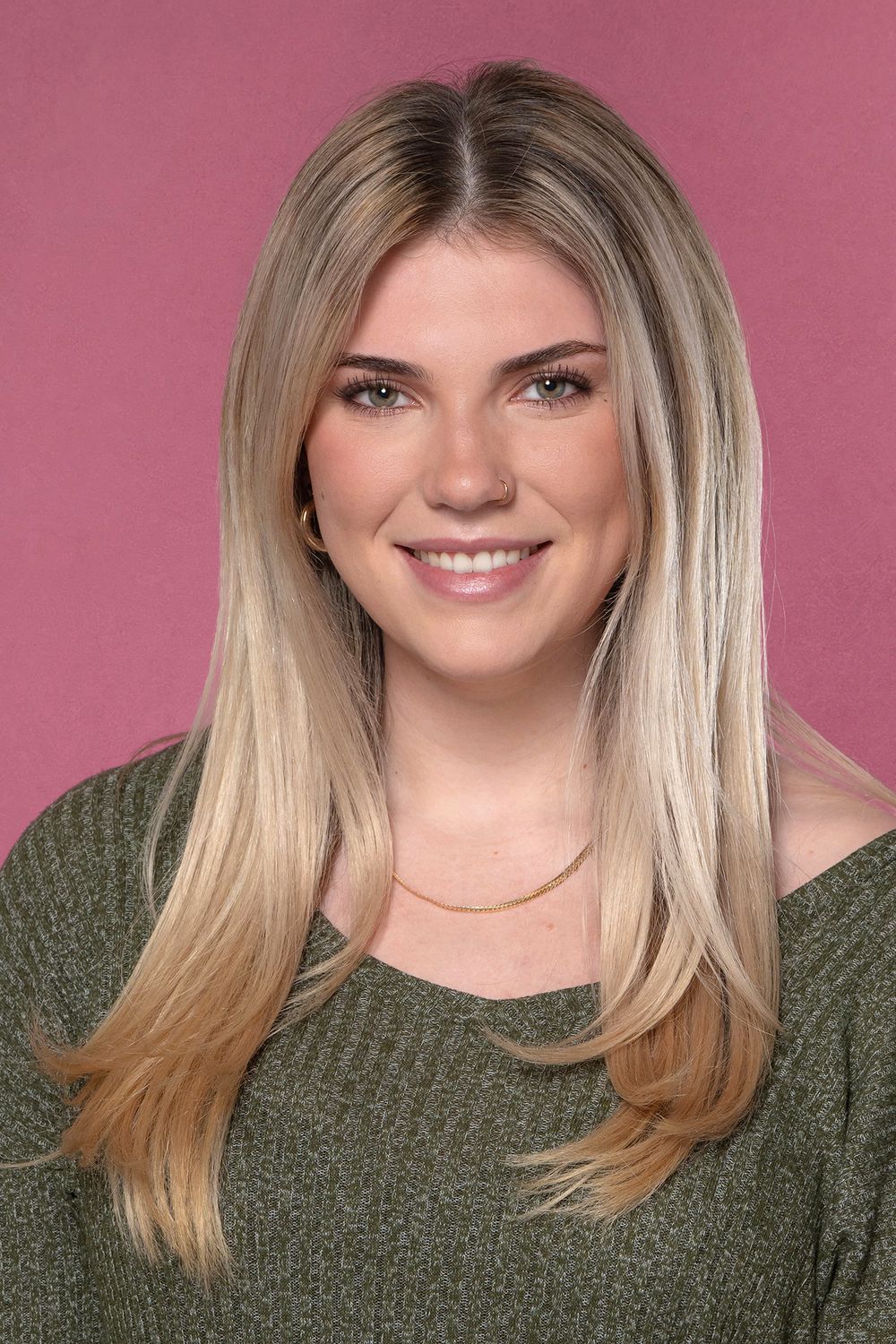 Smiling blonde woman with long hair wearing a green top against a pink background.