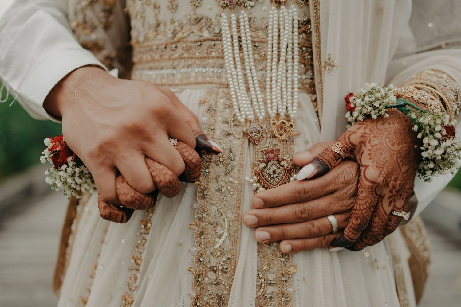 Hands adorned with henna mehndi designs hold delicate baby's breath flowers against an embroidered cream-colored wedding dress.