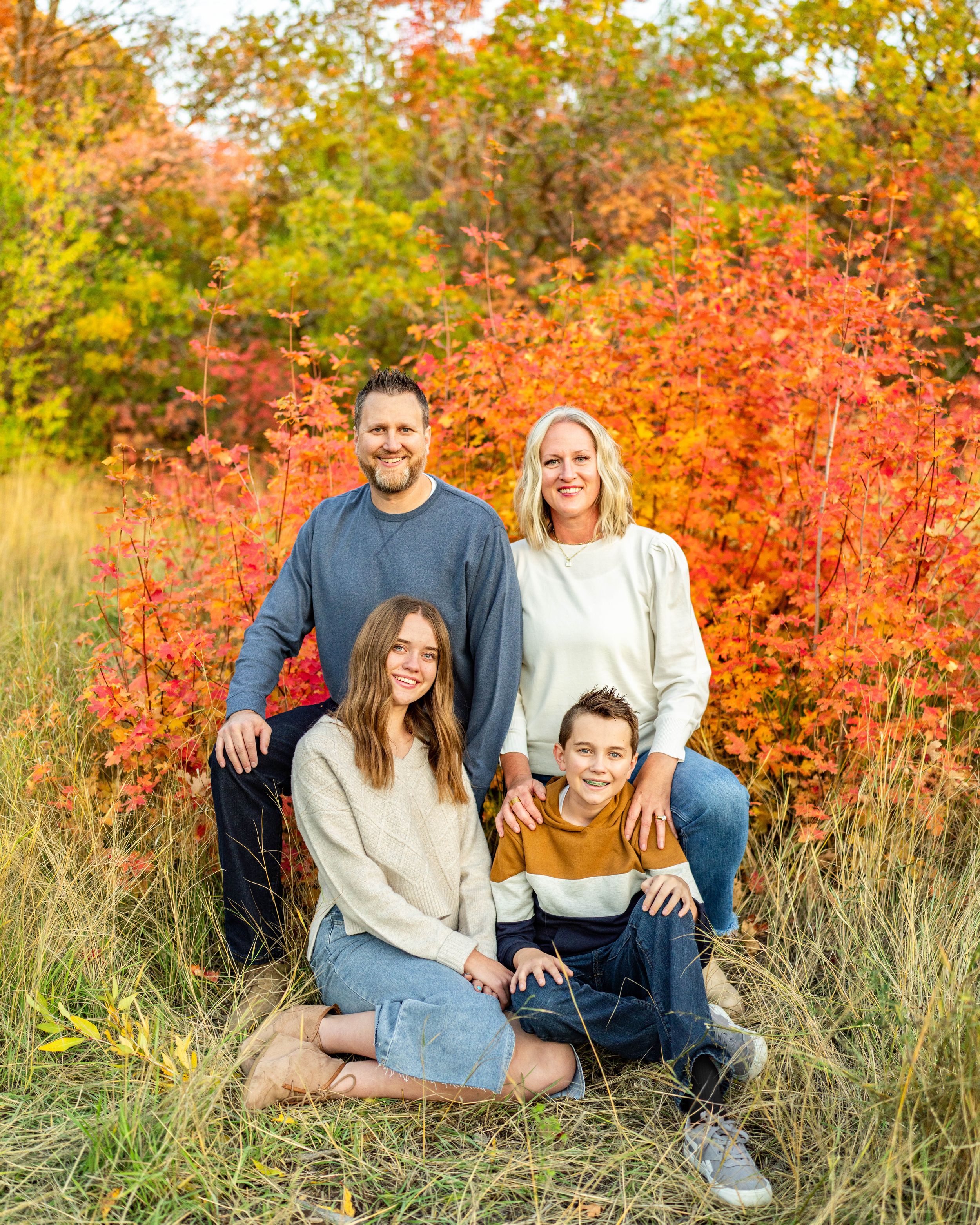 A family of four poses together against vibrant orange and red fall foliage at Neff's Canyon.