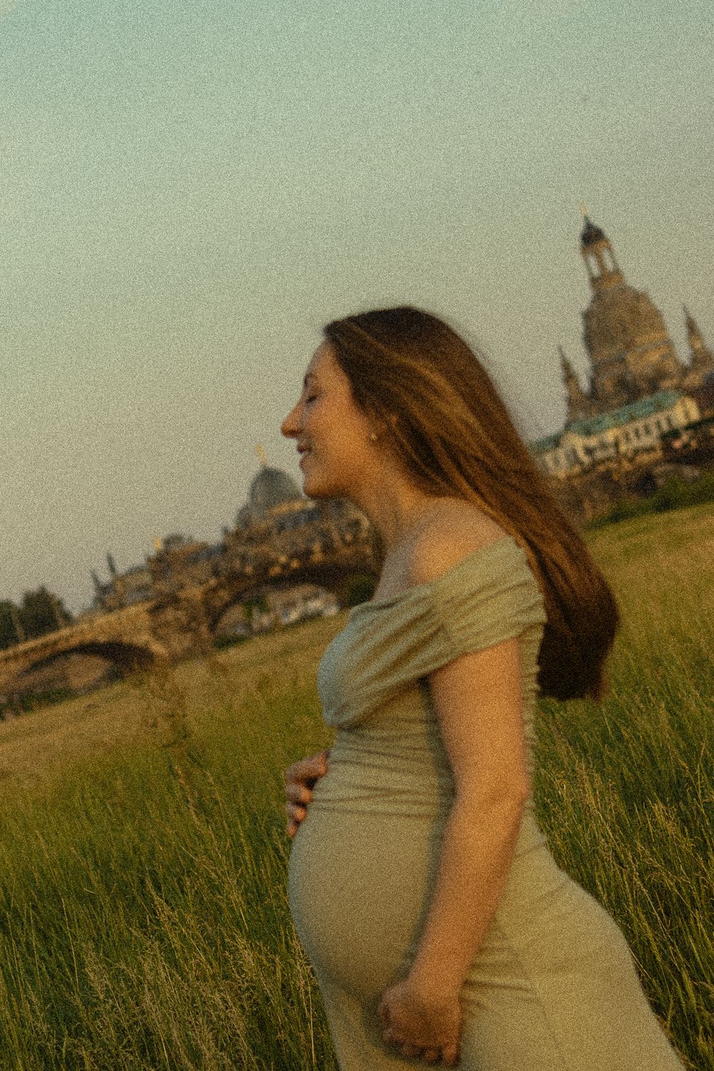 Frau schließt die Augen und neigt Kopf gen Himmel und genießt Augenblick mit ihrem schwangeren Bauch-Fotoshooting Dresden Altstadt Elbwiesen
