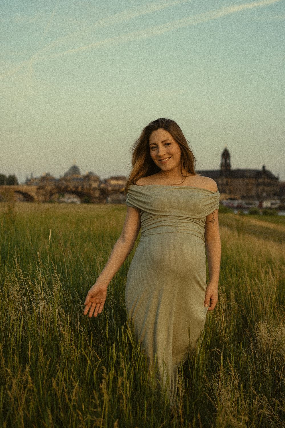 Frau mit schwangeren Bauch läuft im grünen Kleid über Wiese mit Canalettoblick und streicht mit Hand durchs Gras - Portrait Fotoshooting