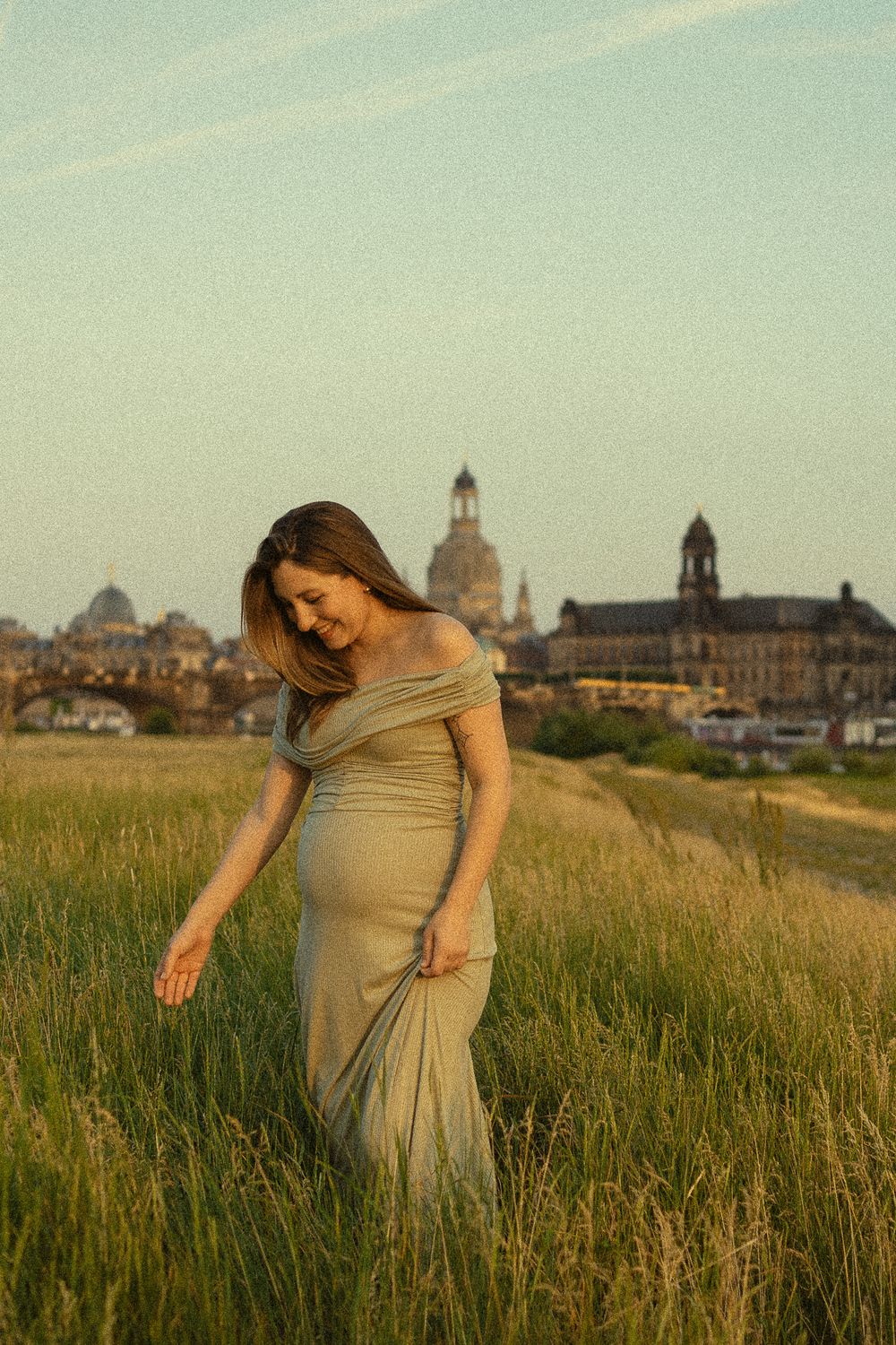 Nostalgisches Babybauchfotoshooting - Schwangere Frau läuft durch Elbwiesen mit Altadt im Hintergrund - Portrait Fotografie Dresden