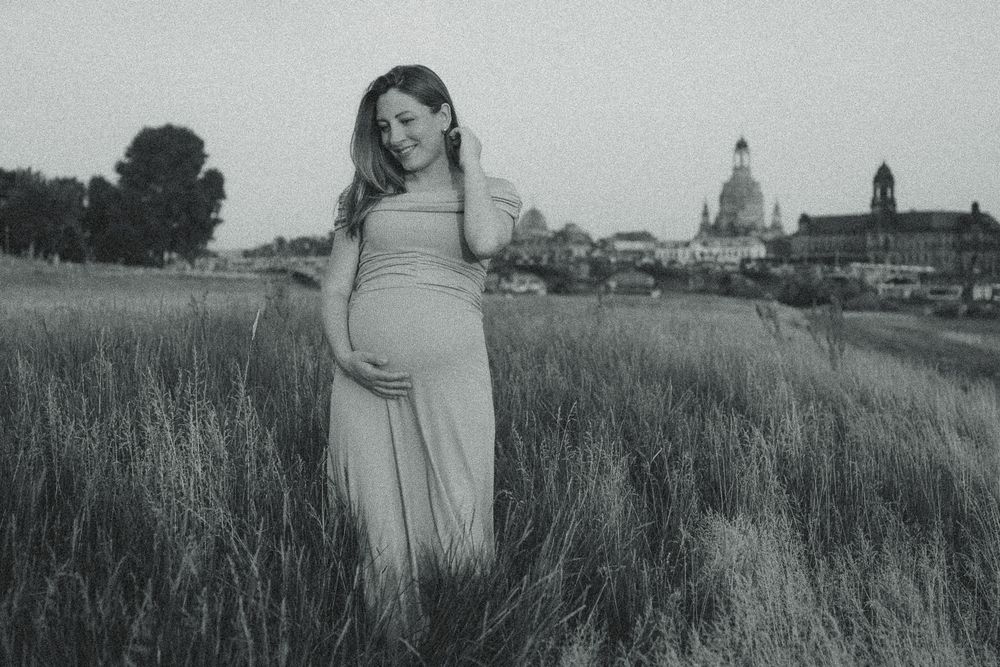 Schwangere Frau spaziert im Kleid über Elbwiesen bei Sonnenuntergang und streicht sich durch Haar - Portrait Fotoshooting mit Canalettoblick