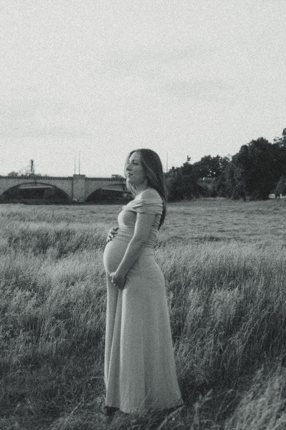 Babybauchfotoshooting - Frau hält sich schwangeren Bauch im warmen Abendlicht der Elbwiesen in Dresden
