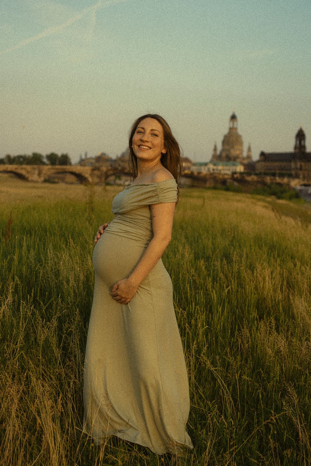 Portrait Fotoshooting Dresden zur goldenen Stunde an den Elbwiesen mit Altstadtbllick im Hintergrund - schwangere Frau lächelt