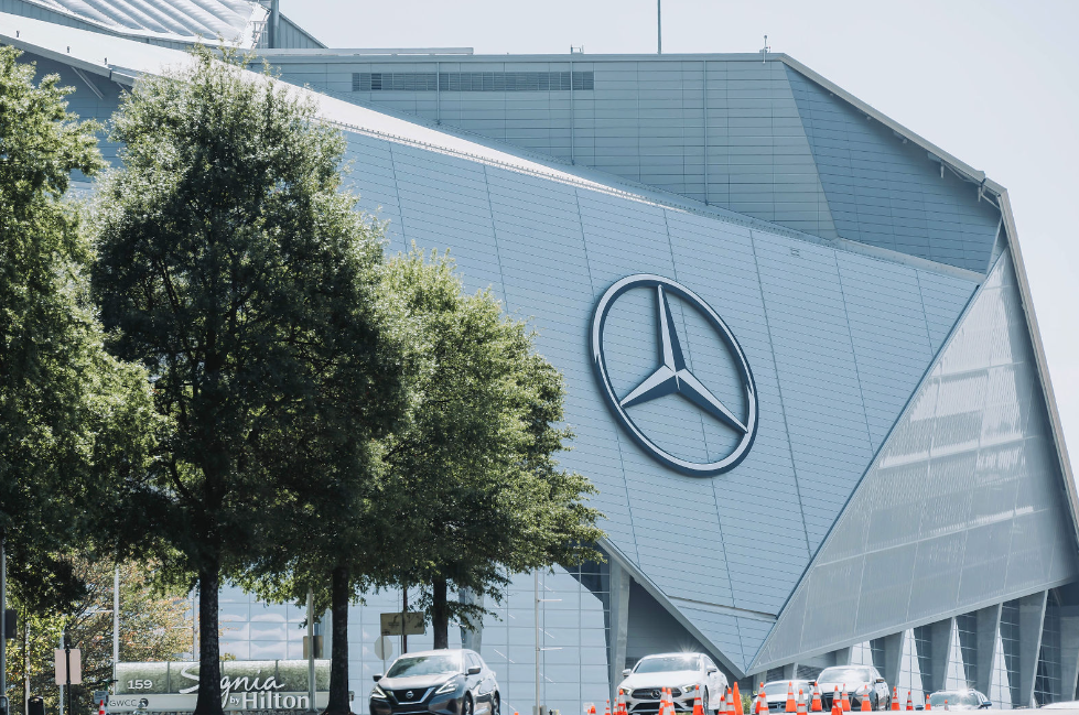 Modern Mercedes-Benz building facade with large logo against blue sky and trees.