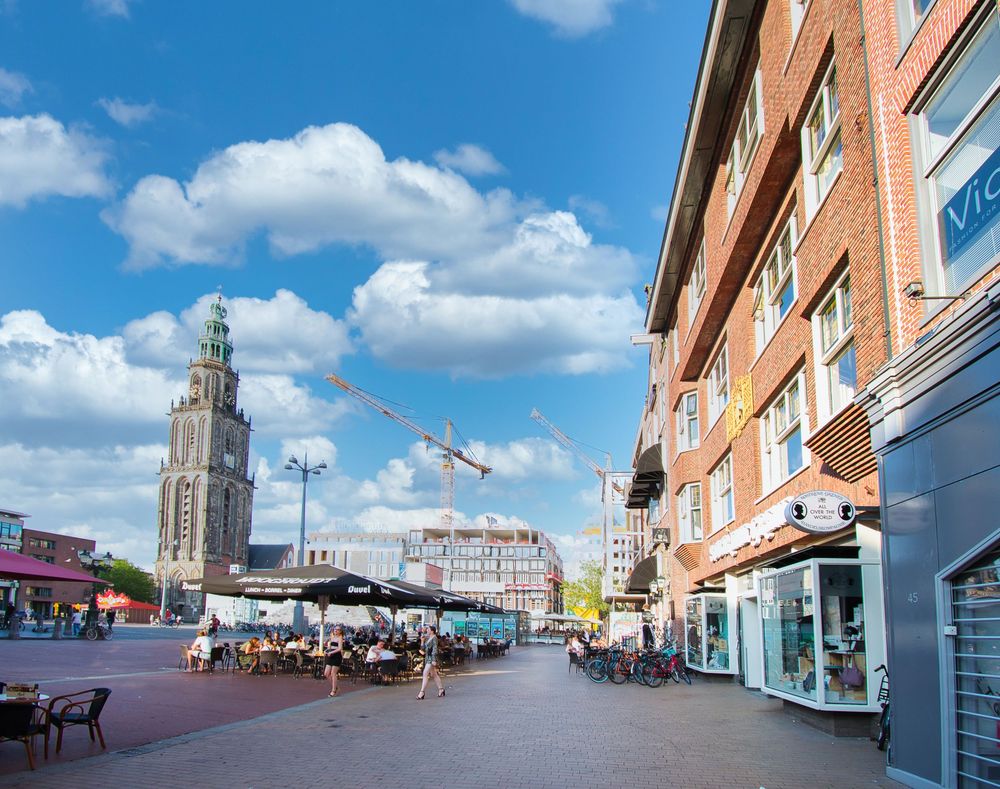 Long brick building with blue sky and white clouds visible in a panoramic view of an urban street scene.