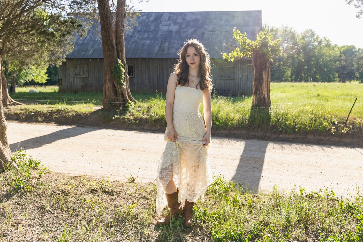 Woman in casual attire walking outdoors in a sunny natural setting with trees and grass in the background.