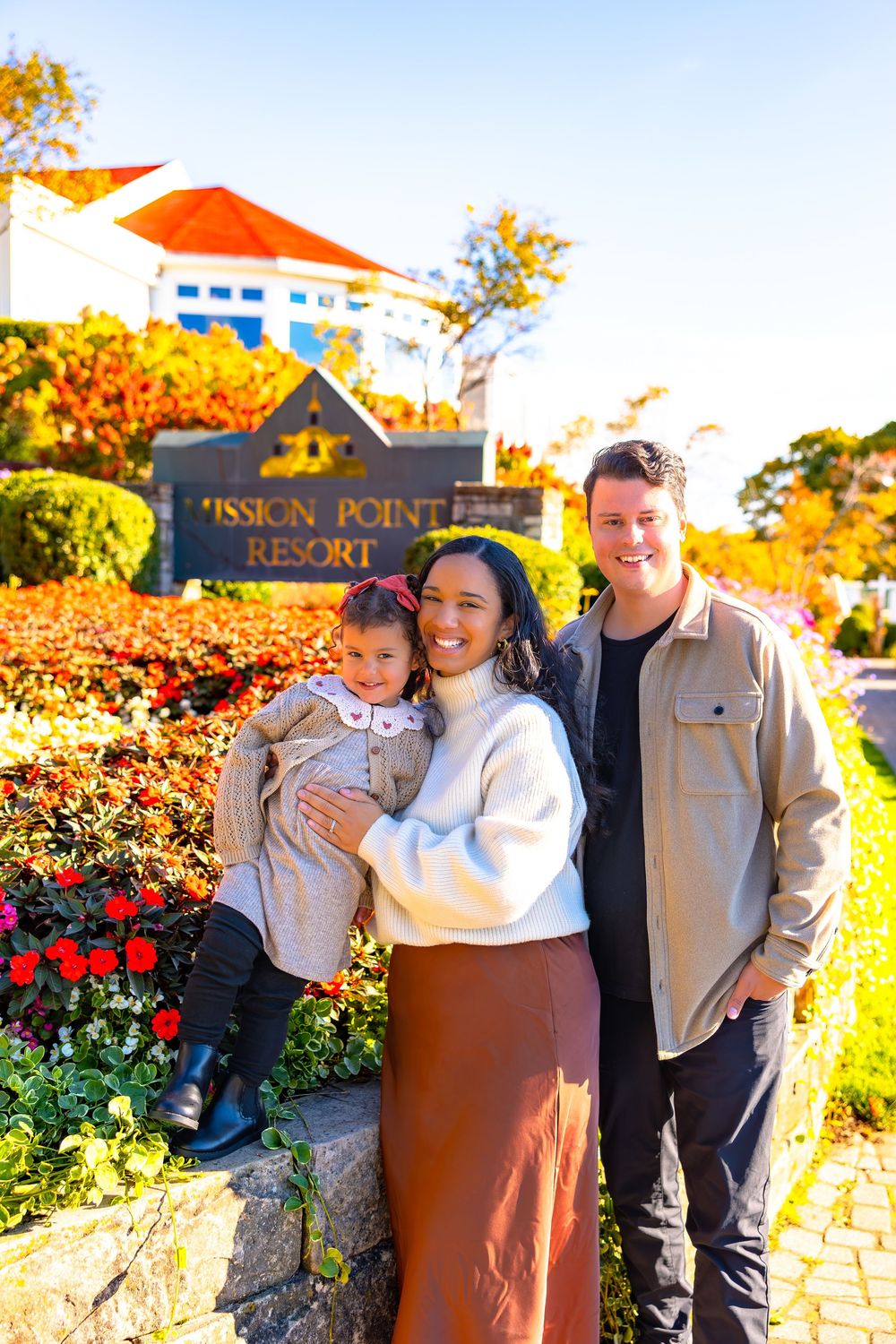 A group poses together for photos in front of Mission Point Resort's stone sign surrounded by colorful autumn foliage.