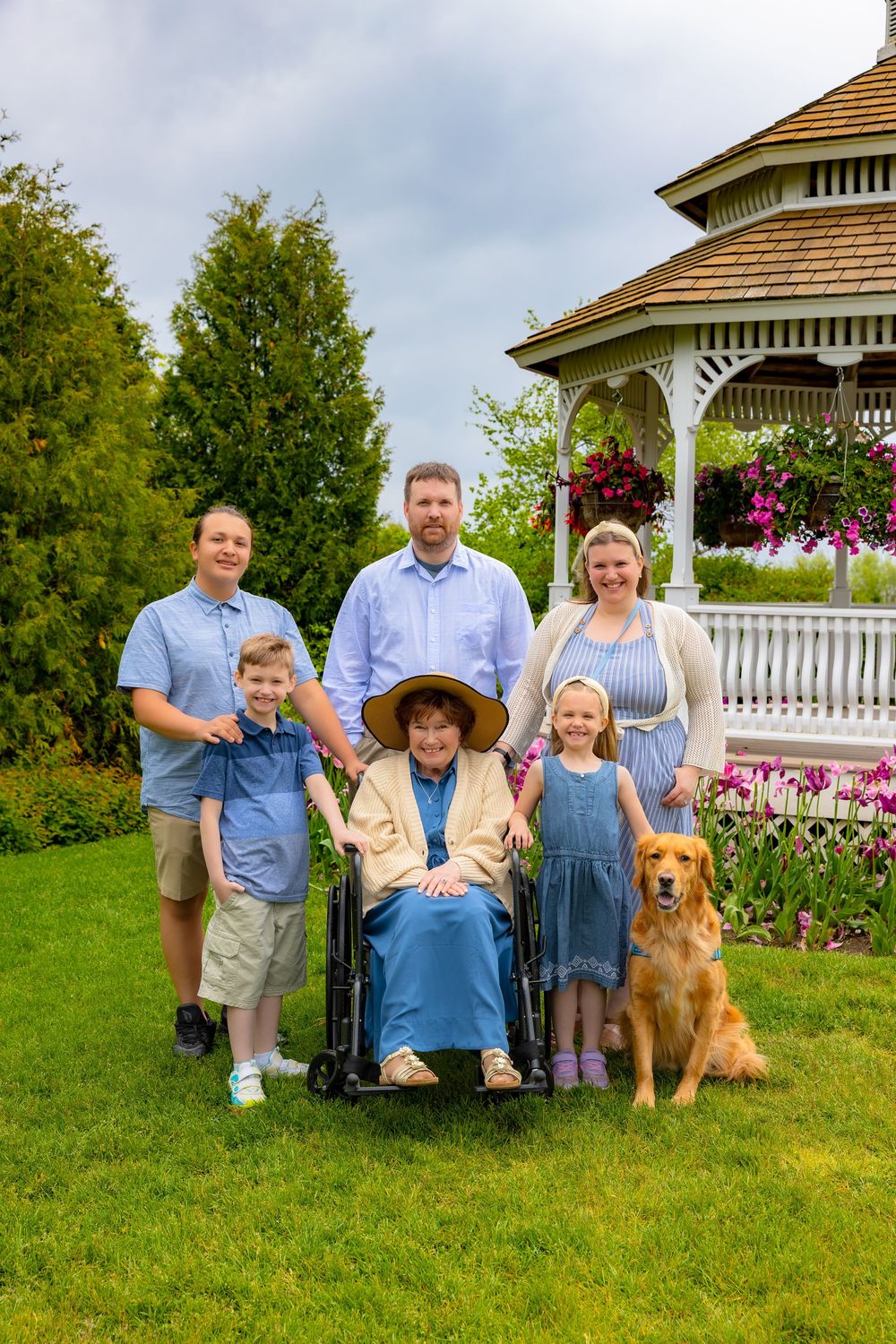 Family poses together with their golden retriever dog in front of a white gazebo with pink flowers in the garden.
