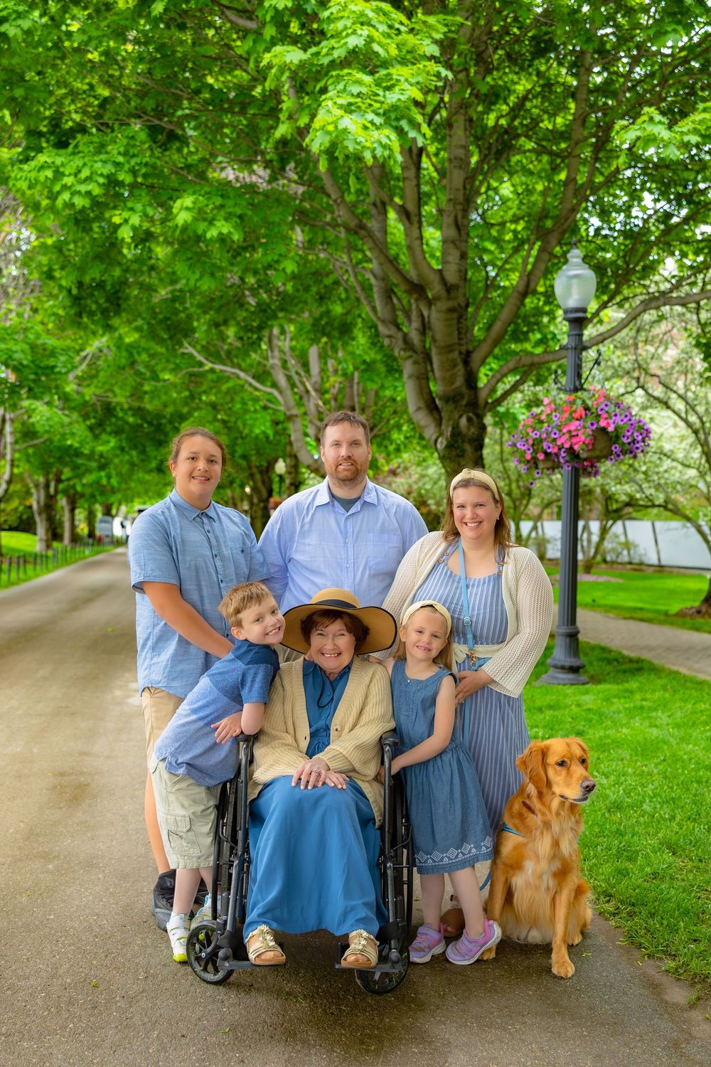 Family in coordinating blue outfits poses together with their golden retriever dog in a lush green park setting.