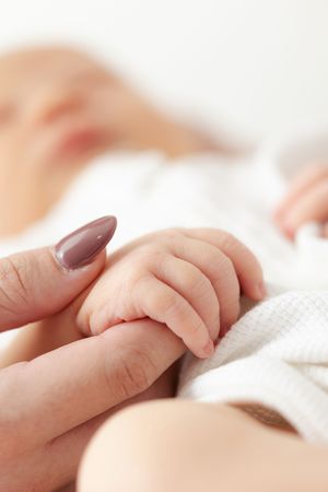 Close up of a tiny baby's hand grasping an adult finger with manicured nails against white bedding.