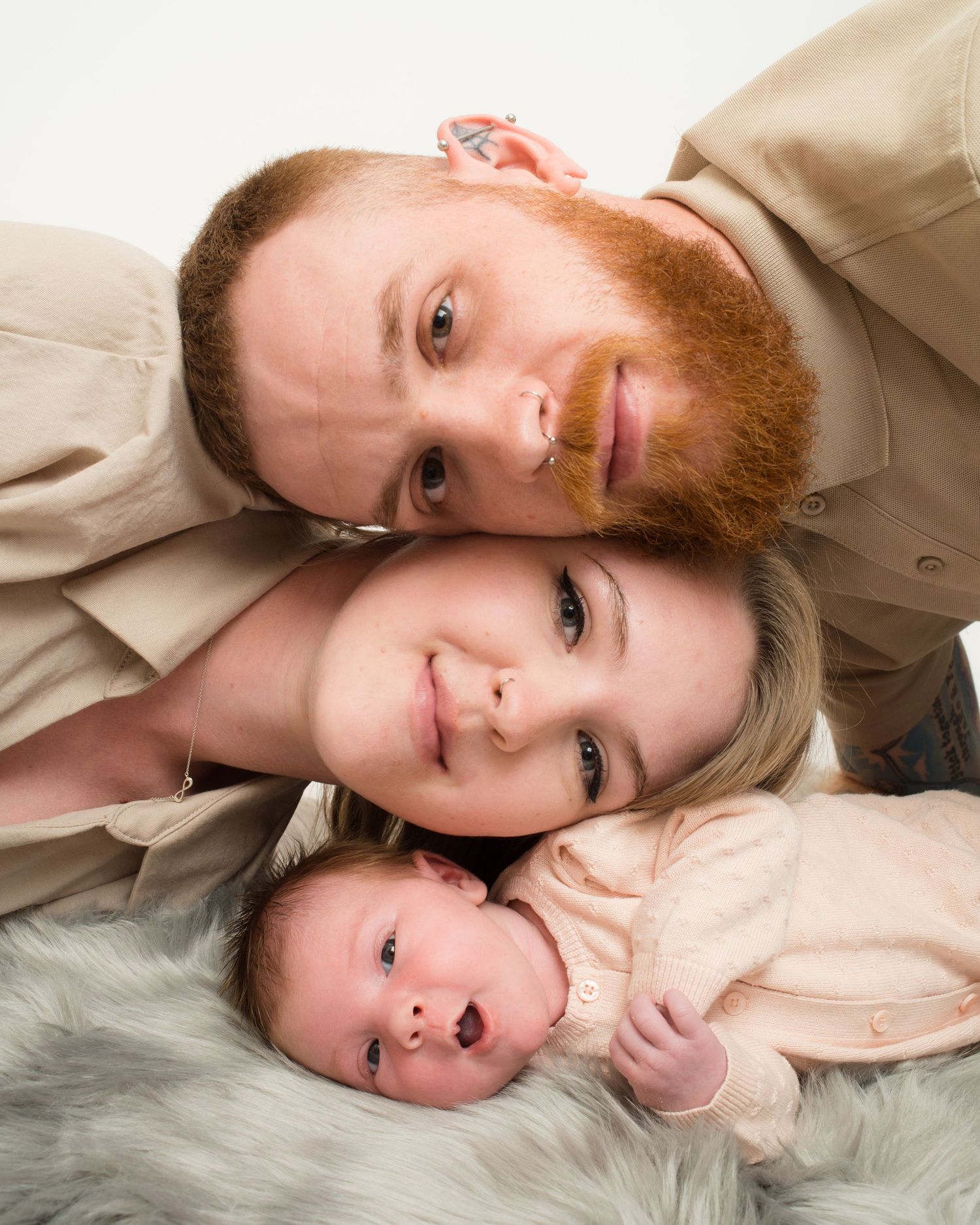 Newborn photography by Abigail's Studio shows a bearded father and young mother gently posing with their baby in Buckinghamshire.