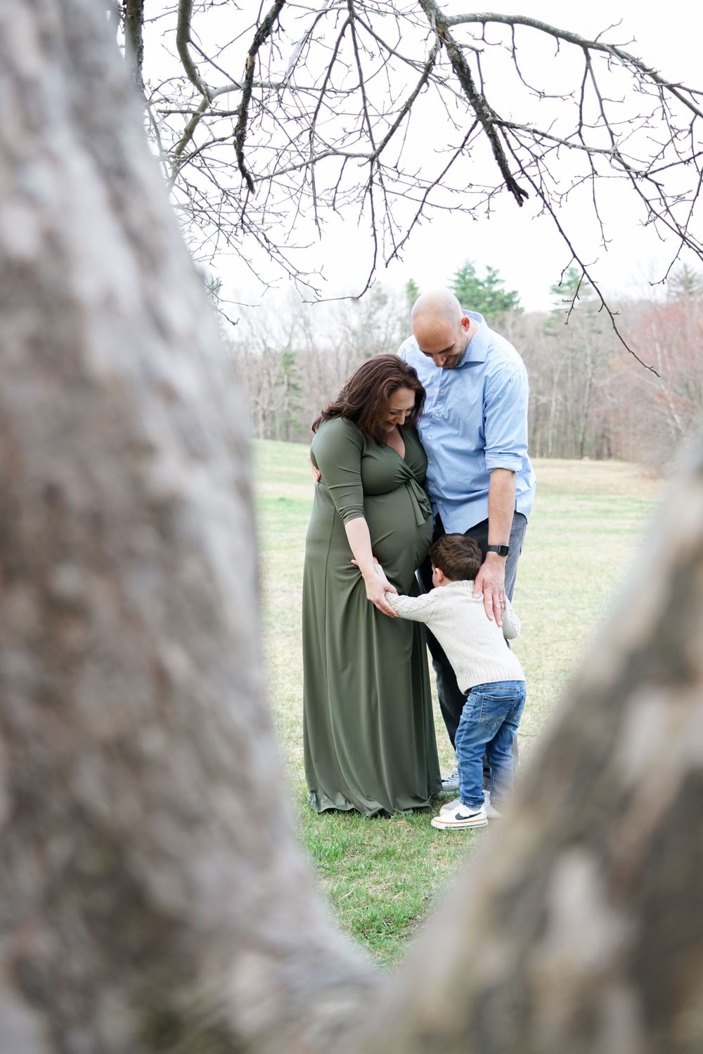 Family shares intimate moment framed by tree branches in outdoor setting.