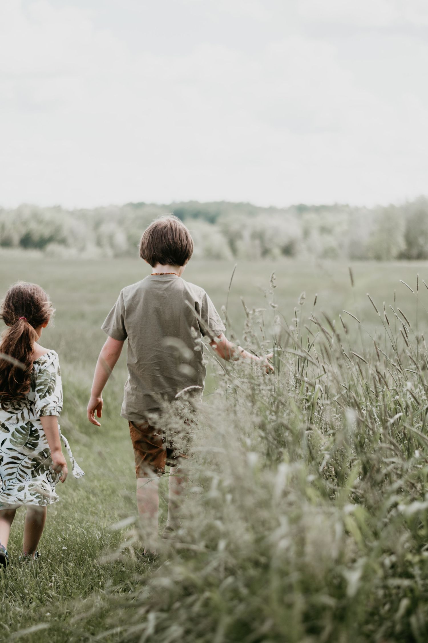 Two children walk through tall grass in a peaceful rural field on a summer day.