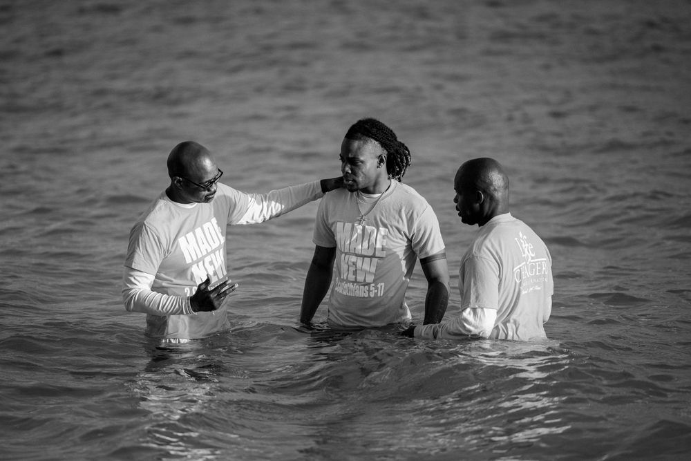 Three men standing in ocean water during a baptism ceremony, black and white photography.
