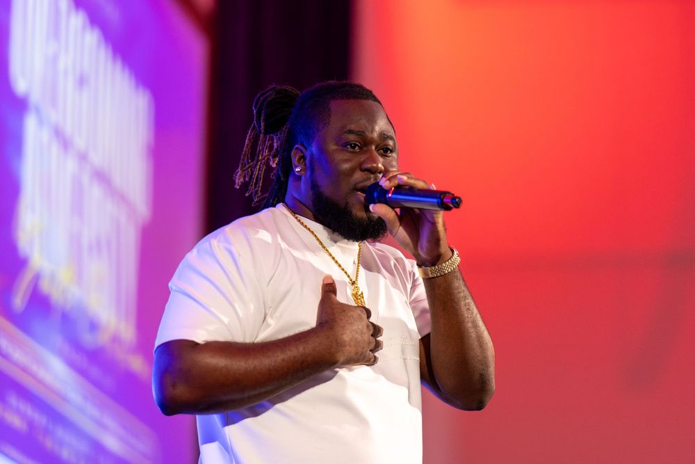 A performer sings into a microphone against colorful stage lighting.