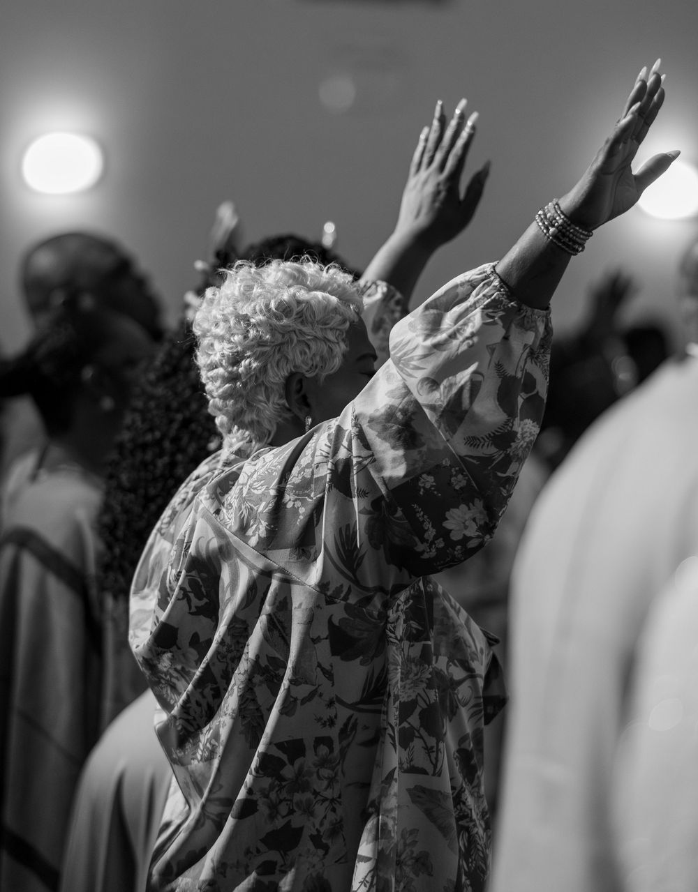 A person raises their hands in worship during a church service, captured in black and white.