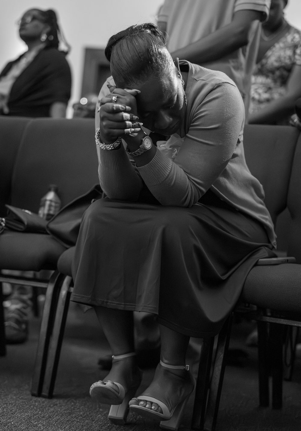 A person bows their head in prayer while sitting in a church pew, shown in black and white.