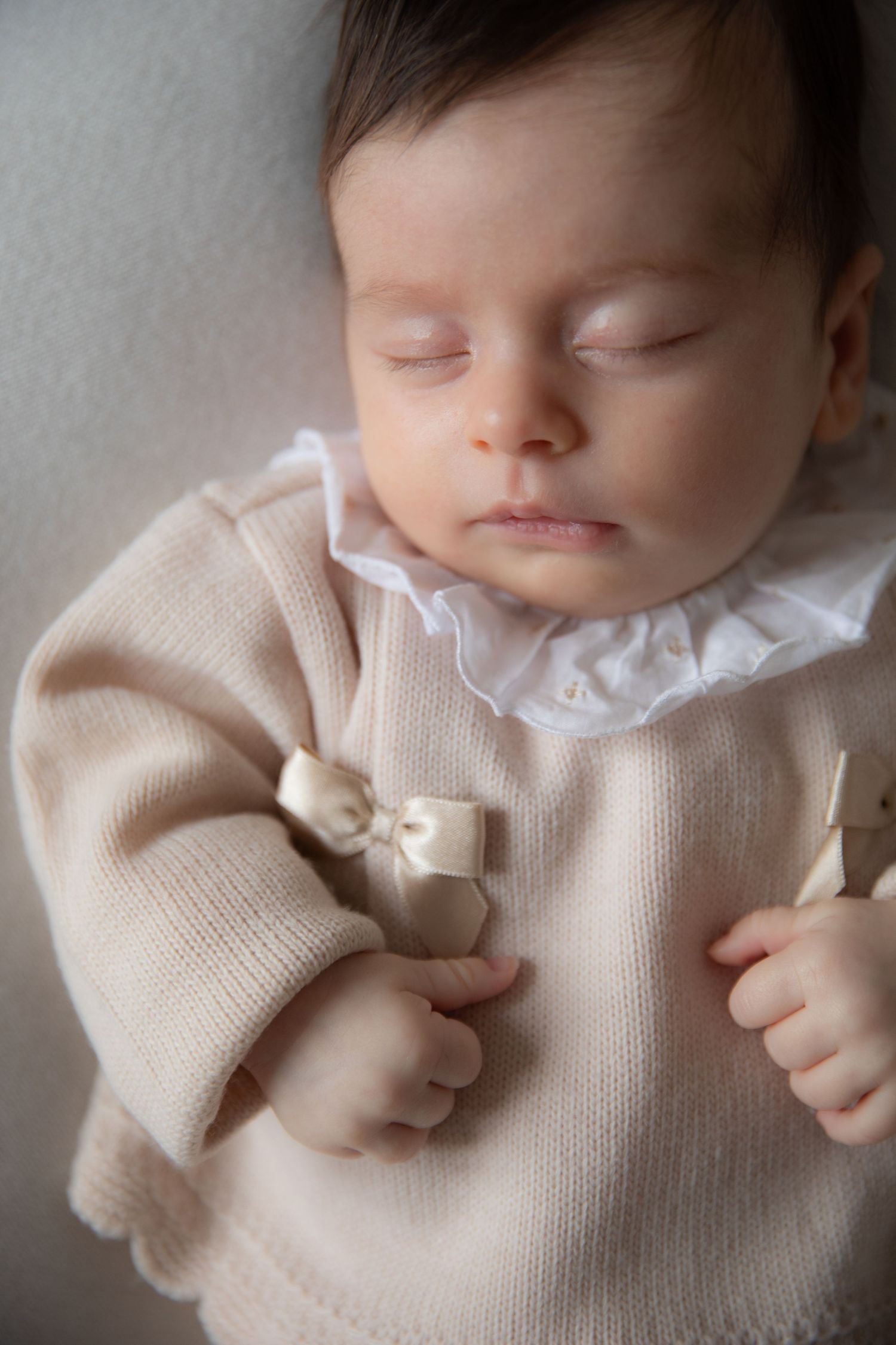 Sleeping baby wearing a soft knit cream sweater with delicate bow details and white collar.