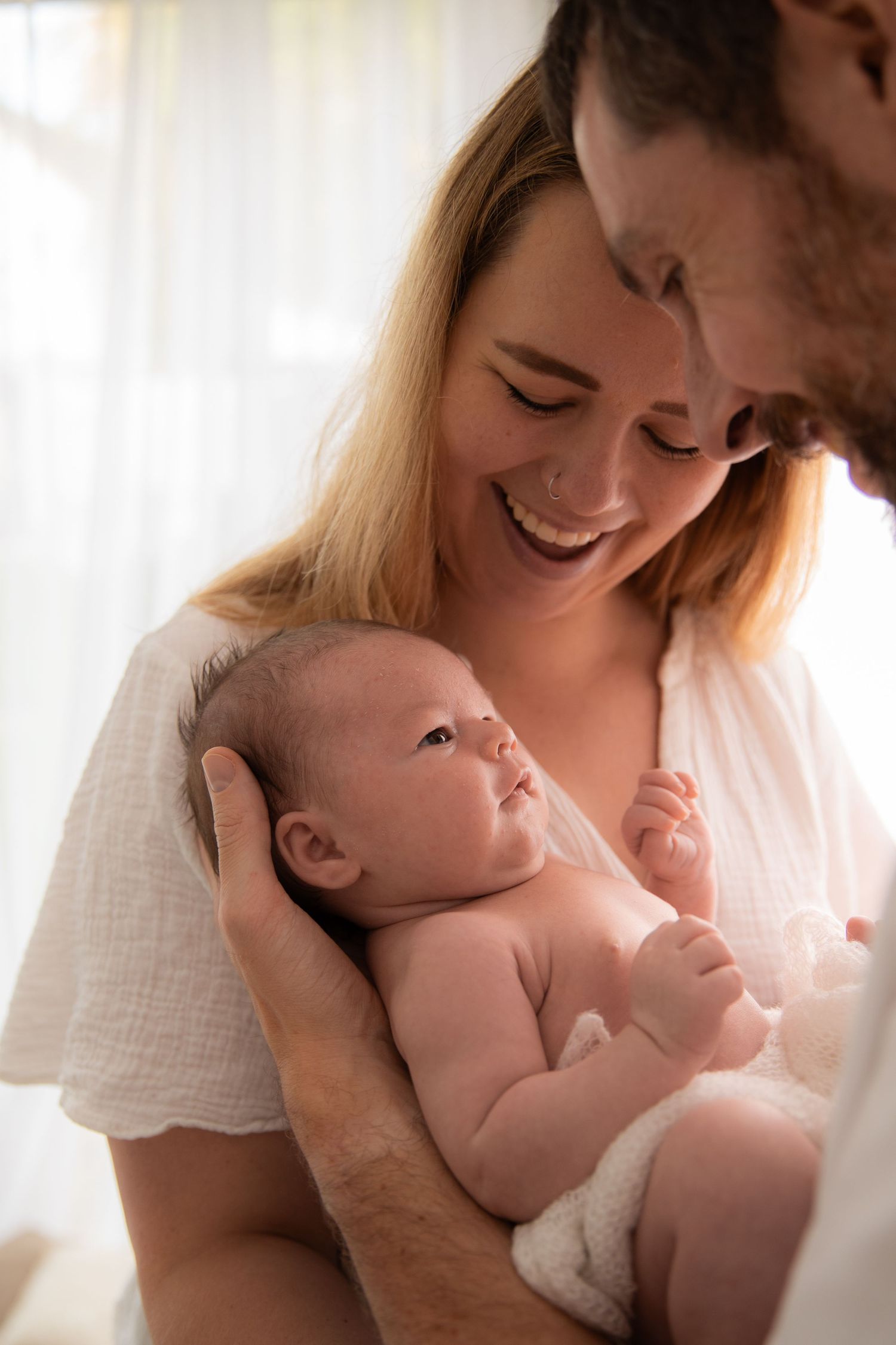 A tender moment between parents and their newborn baby in a bright sunlit room.