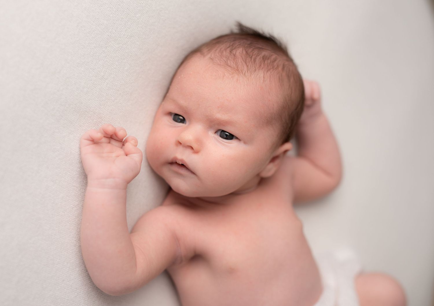 A sleeping newborn baby lies peacefully on soft white bedding during a professional photo session.