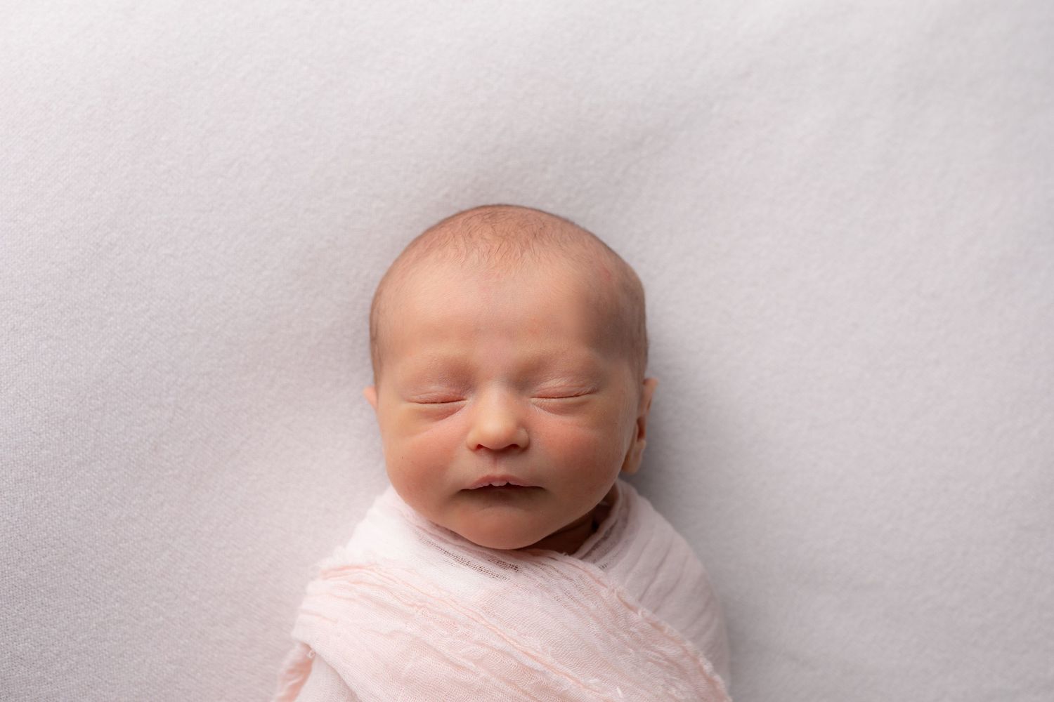 Peaceful newborn baby wrapped in soft pink blanket sleeping on white background.